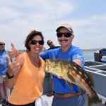 Woman posing with boat captain and fish on fishing charter boat