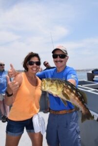 Woman posing with boat captain and fish on fishing charter boat
